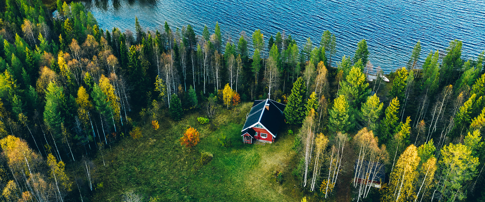 Aerial top view of red log cabin or cottage with sauna in spring forest by the lake in rural Finland