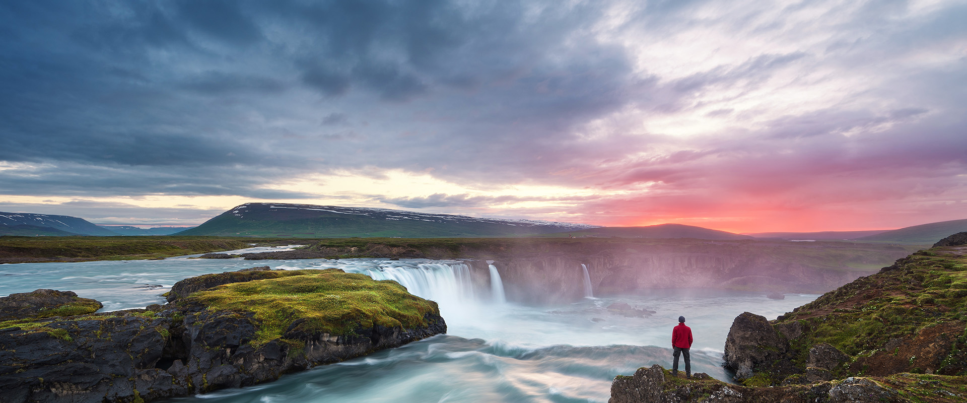 Godafoss waterfall. Beautiful landscape in Iceland. Man in red jacket standing on the rock and looking at the dawn