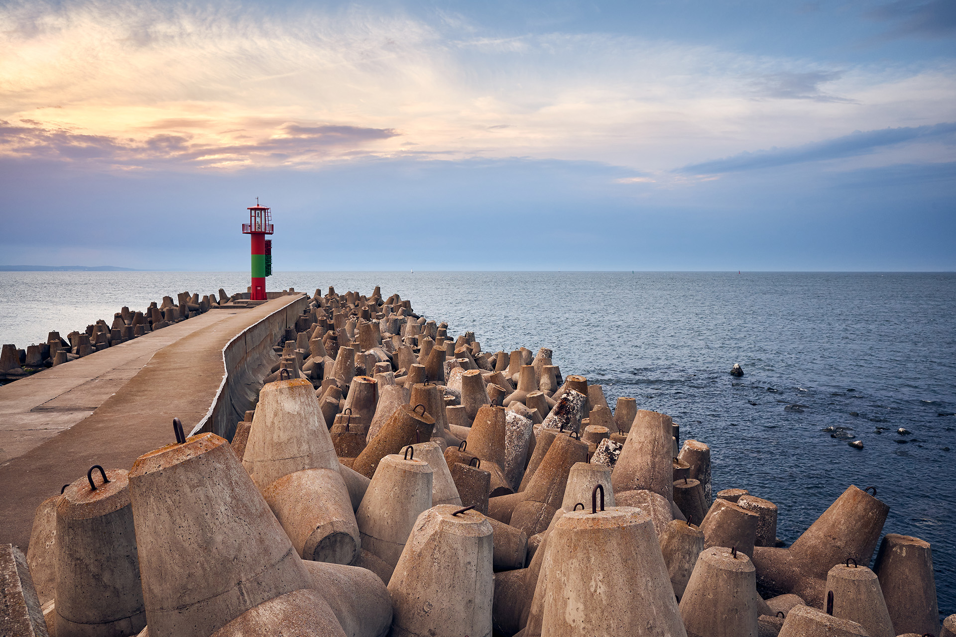 Pier with lighthouse protected by concrete breakwater tetrapods at sunset.