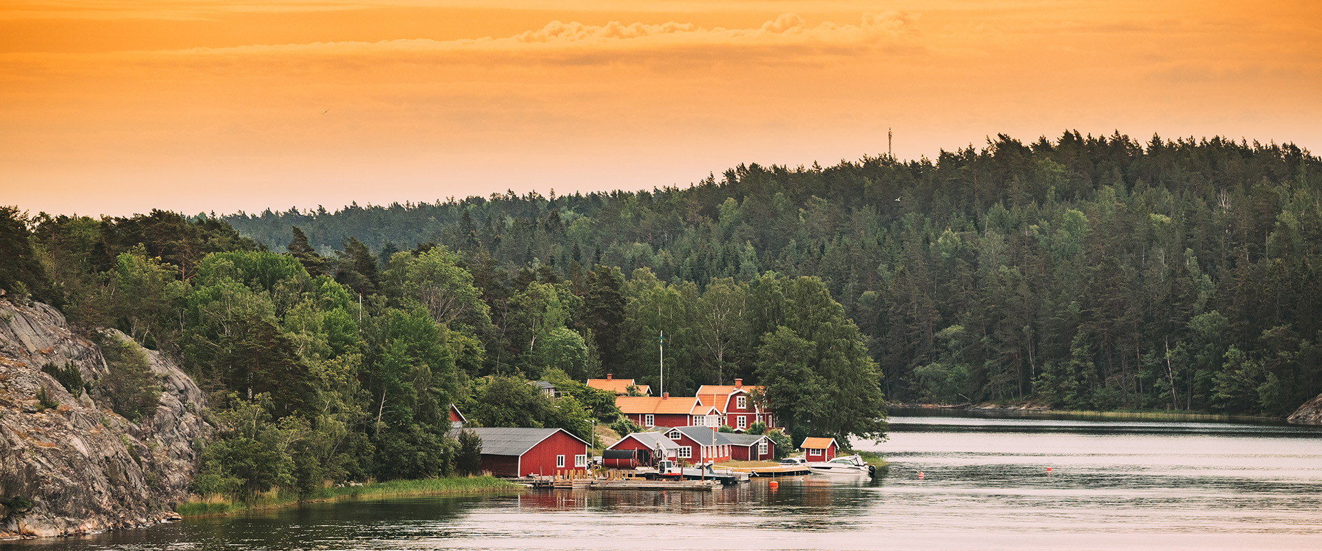 Sweden. Many Beautiful Red Swedish Wooden Log Cabins Houses On Rocky Island Coast In Summer Evening. Lake Or River Landscape.